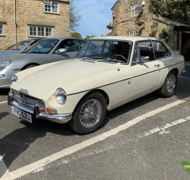 A creamy white MG MGB GT with wire wheels, parked on a street.