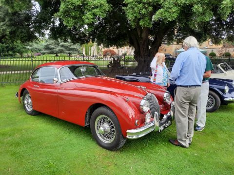 Jaguar XK140 Fixed Head Coupe in red parked on grass.