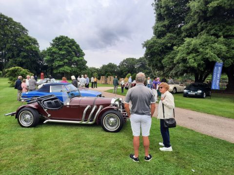 A maroon Morgan Plus 8 convertible at a classic car show with people gathered around.