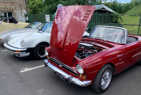 A red Triumph Spitfire GT6 with the hood lifted.