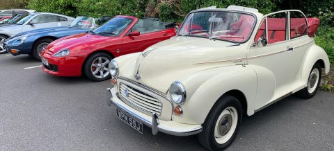 White Morris Minor Convertible parked in a row of classic and modern cars.