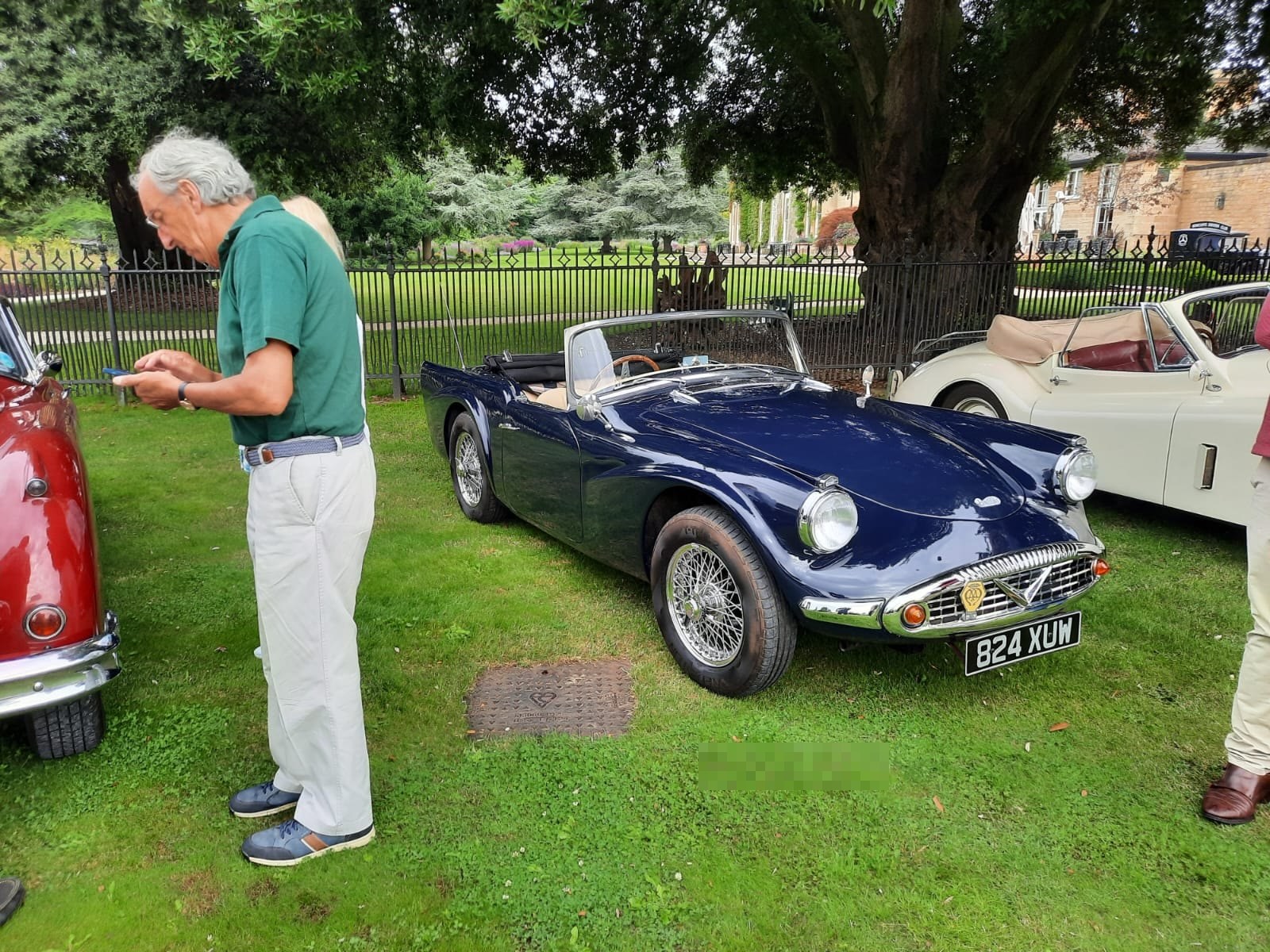 Classic blue convertible car parked in a grassy area with people nearby.
