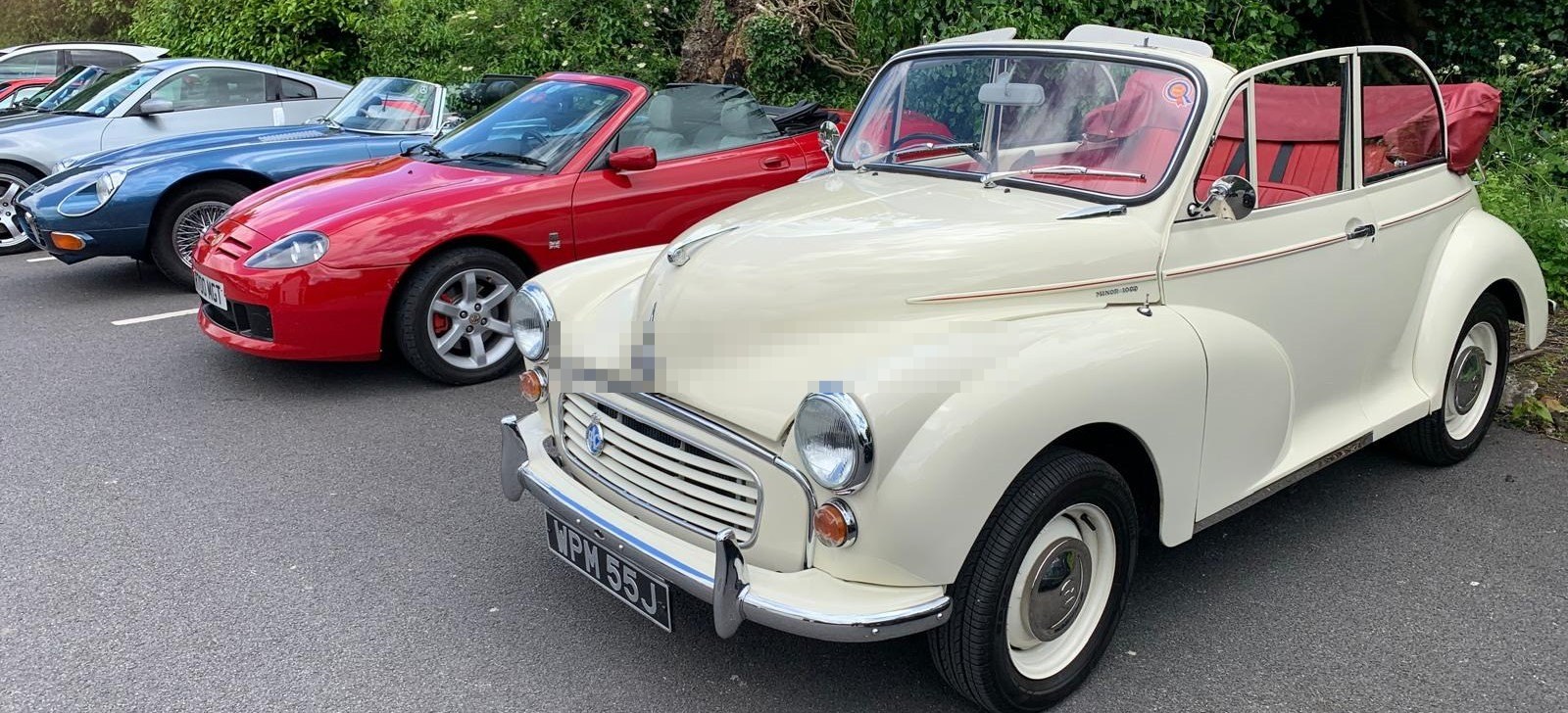 White Morris Minor Convertible parked in a row of classic and modern cars.